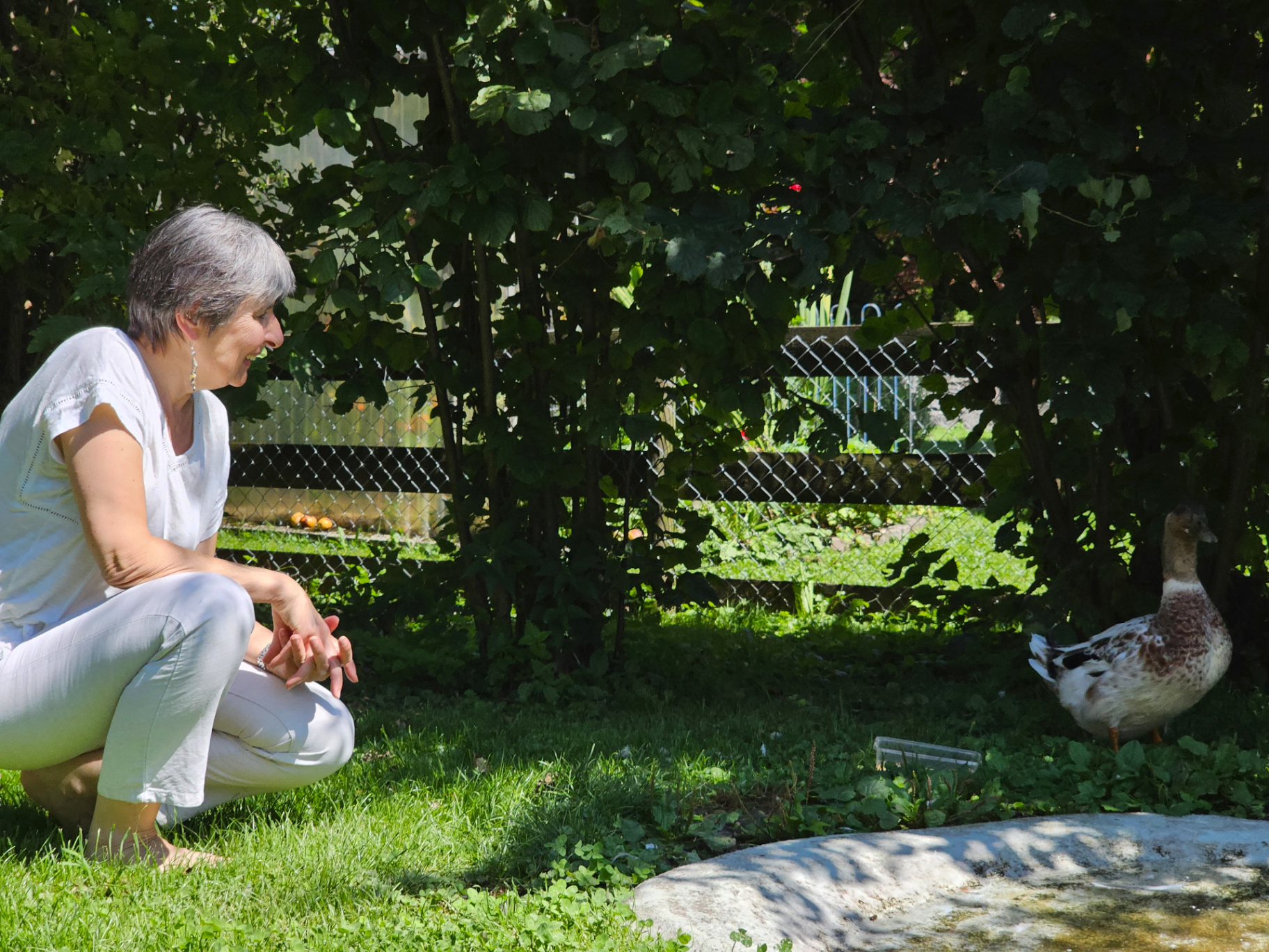 Andrea Beck kniet lachend im Gras und begegnet einer Ente