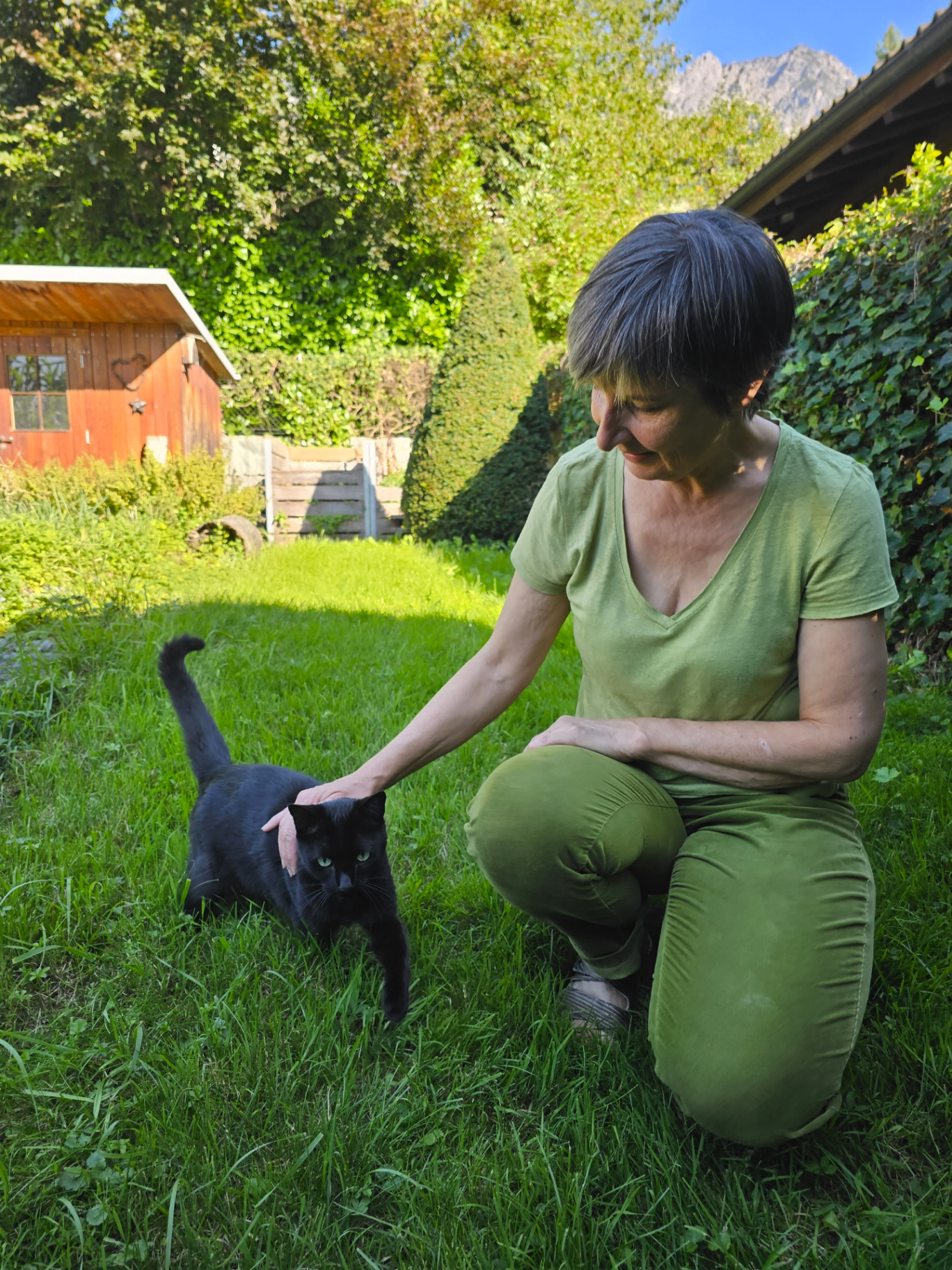 Andrea Beck lacht sanft und streichelt eine schwarze Katze im Garten