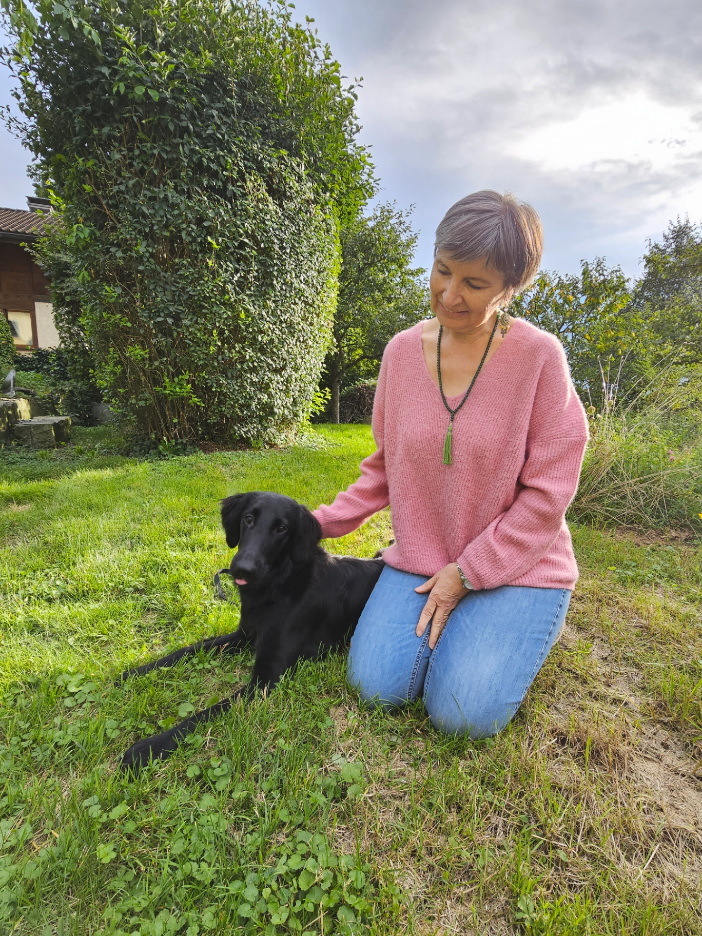 Andrea Beck sitzt ruhig neben einem schwarzen Hund im Garten