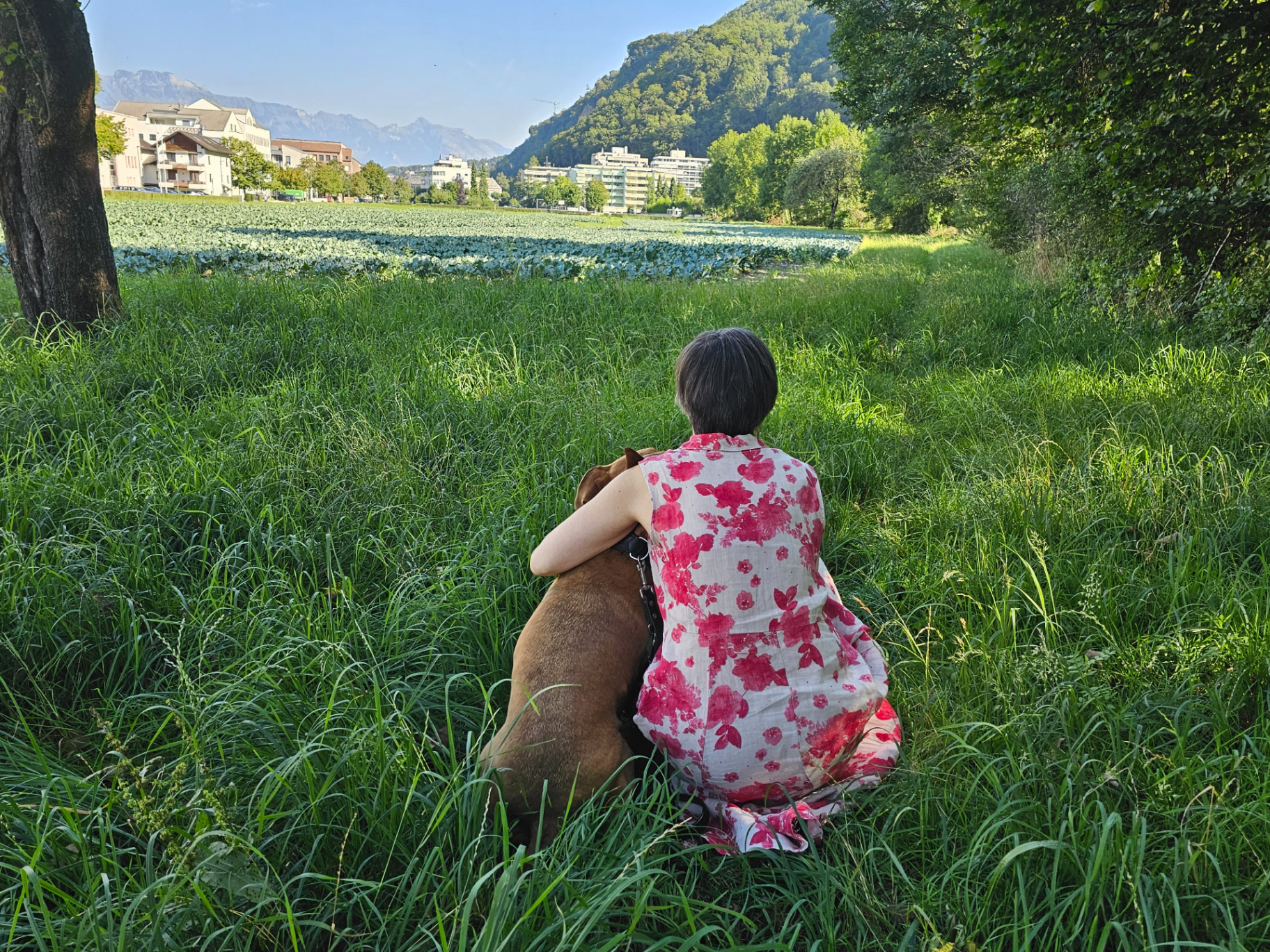 Andrea Beck sitzt still im hohen Gras neben ihrem Hund